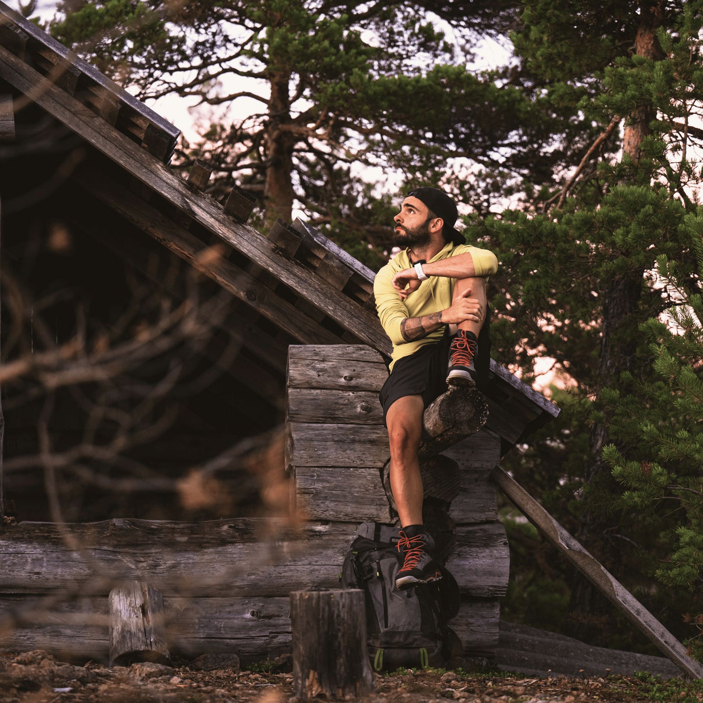 a man sitting on a cabin holding his leg, gazing into the forest 