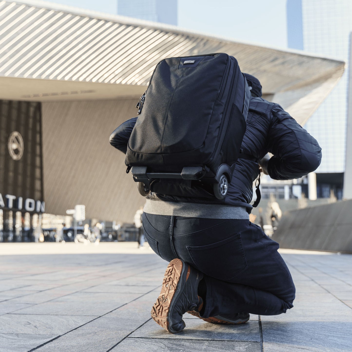 A man crouching down, view from the backside, wearing a roller backpack