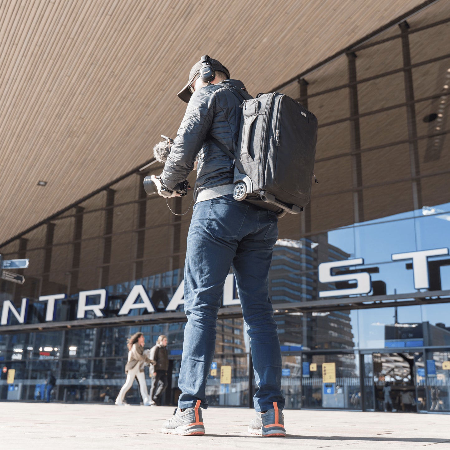 A man wearing a roller backpack, holder camera equipment and wearing headphones