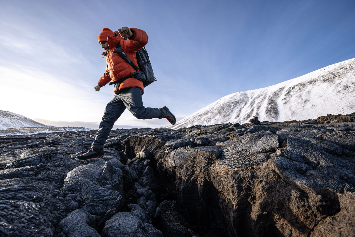 A man in mid-air wearing a backpack, jumping from a rock  