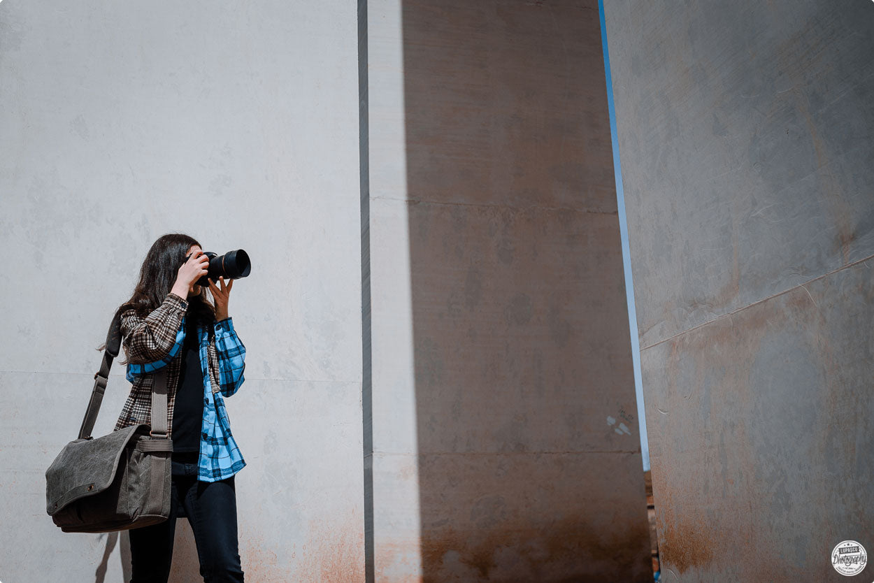 A women, holding the camera to her face, wearing a messenger bag 