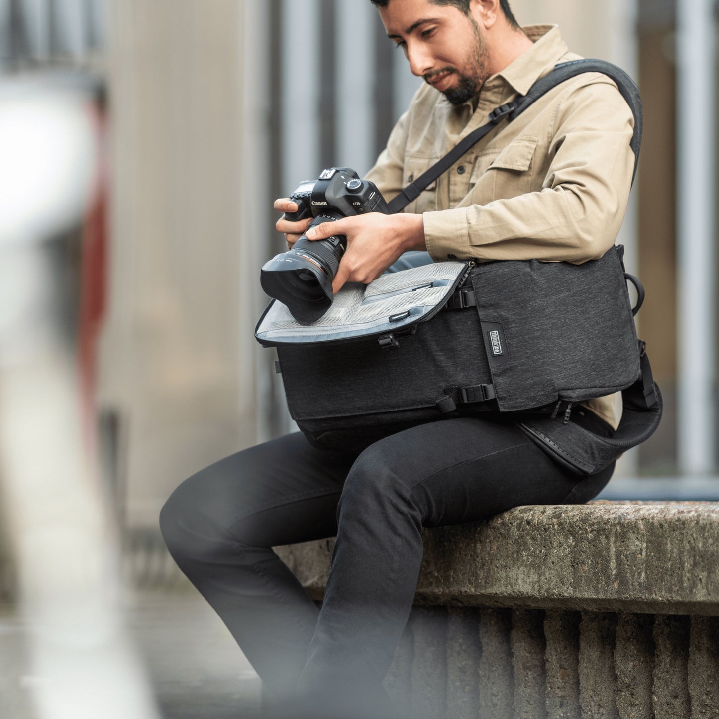 A photographer sitting on a ledge, looking through his camera propped on a small camera bag