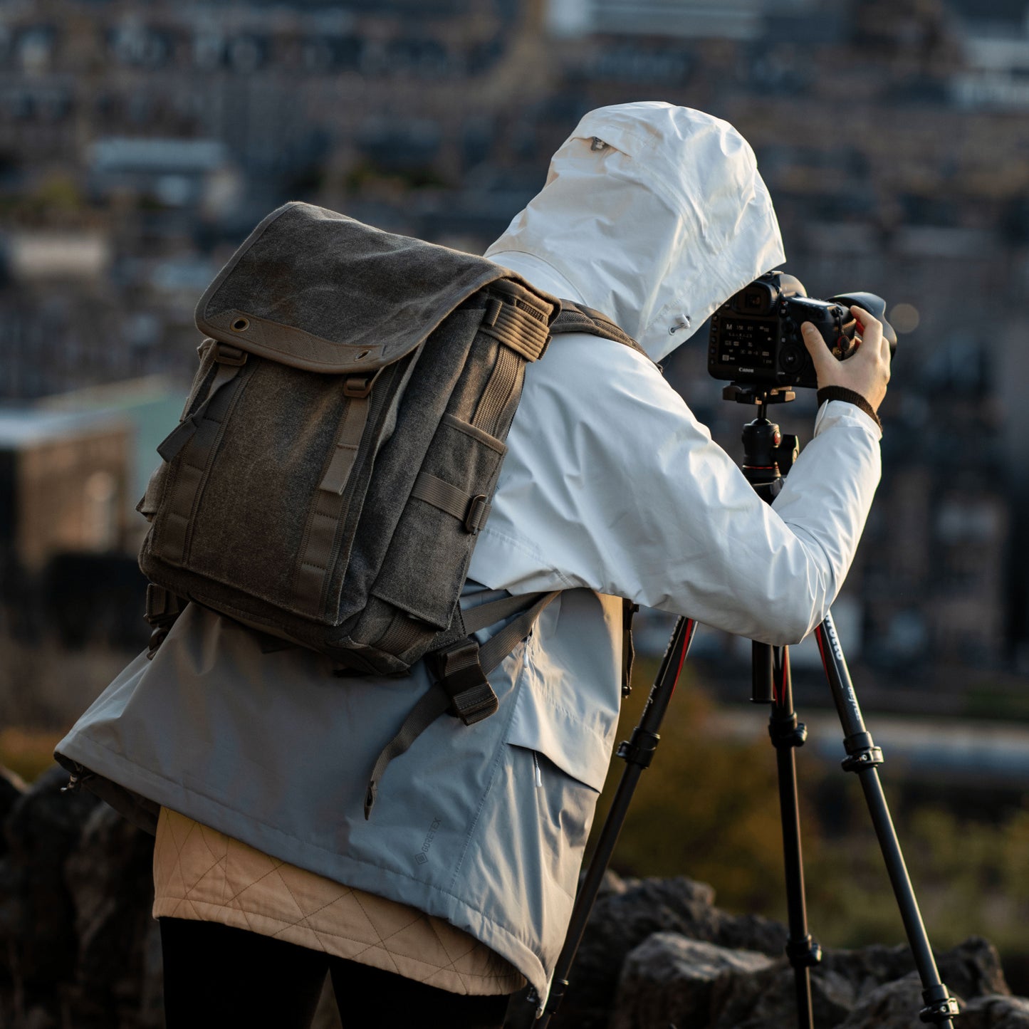 A photographer standing, wearing a backpack in front of a camera on a tripod.