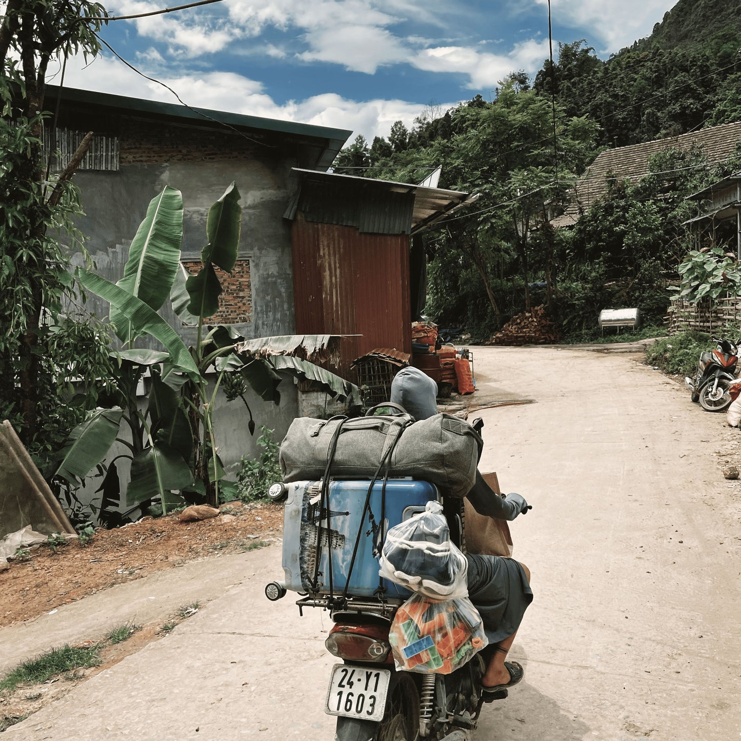 A person riding a moped, with several luggage strapped in 